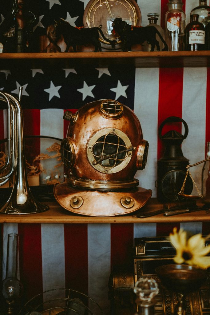 A retro diving helmet on a shelf with an American flag in the backdrop, creating a vintage feel.